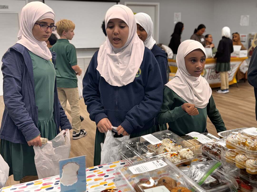 Students in green uniforms browse the cupcake table together