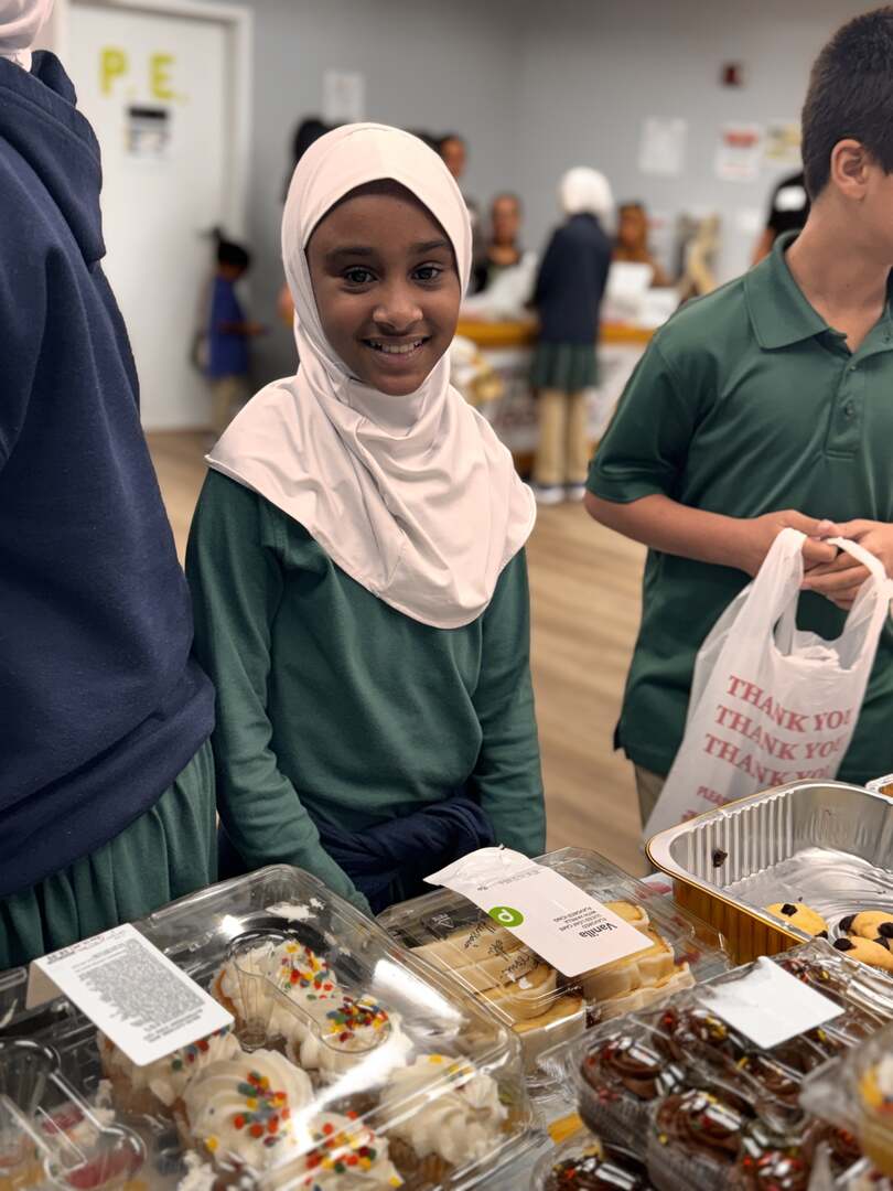 A student smiles brightly over a table of cupcakes