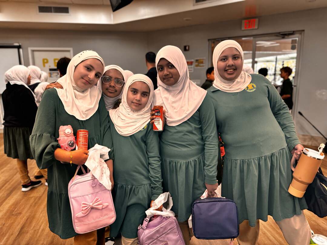 A cheerful group of students gathers close with their drinks and lunch bags