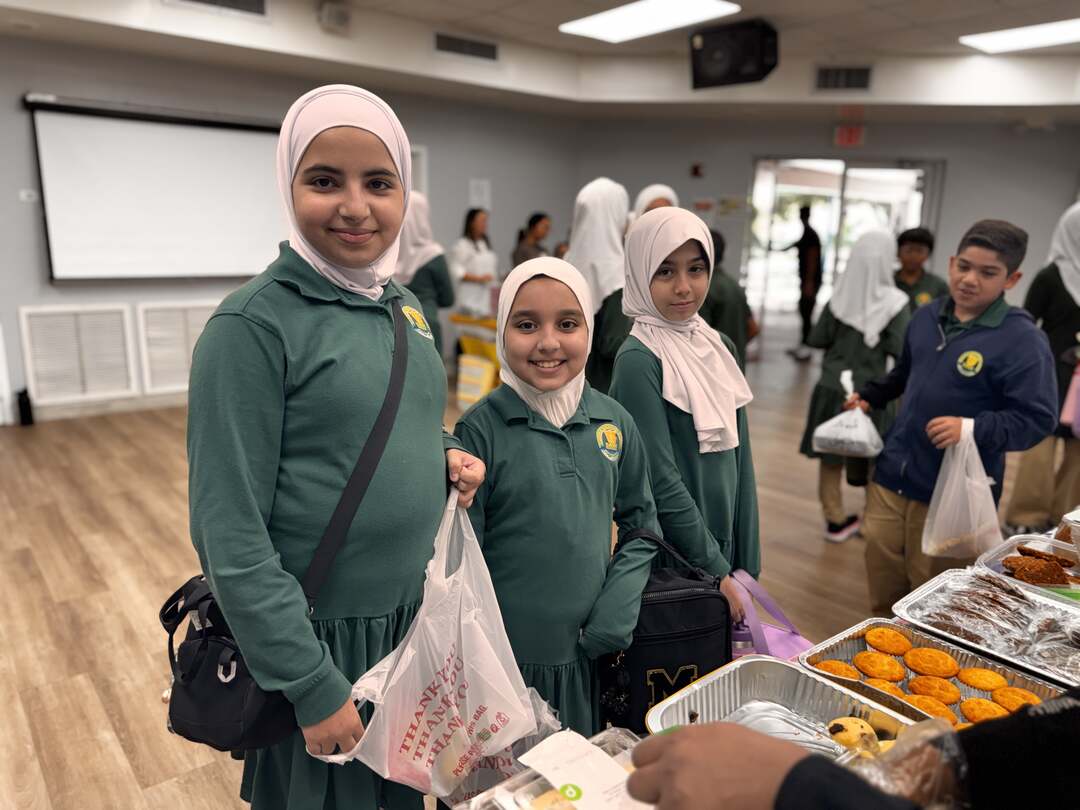 Three smiling students in green uniforms stop by the dessert table