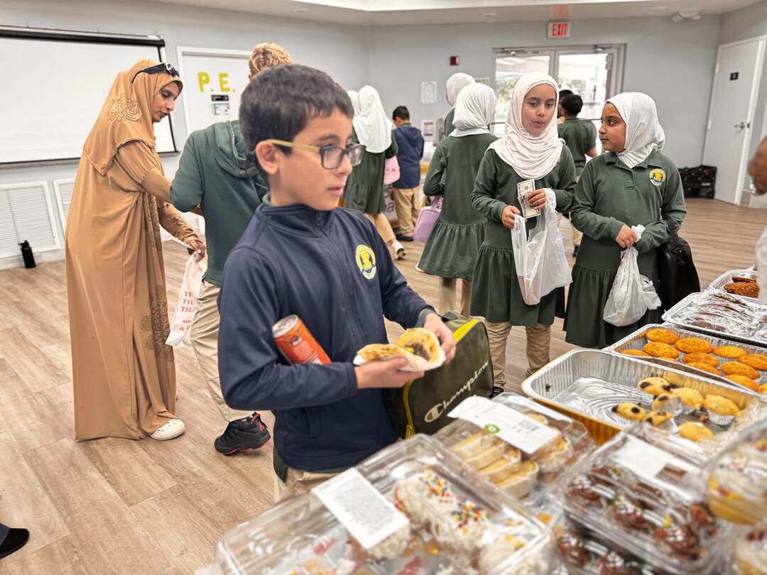 A student in glasses chooses a treat while classmates mingle nearby