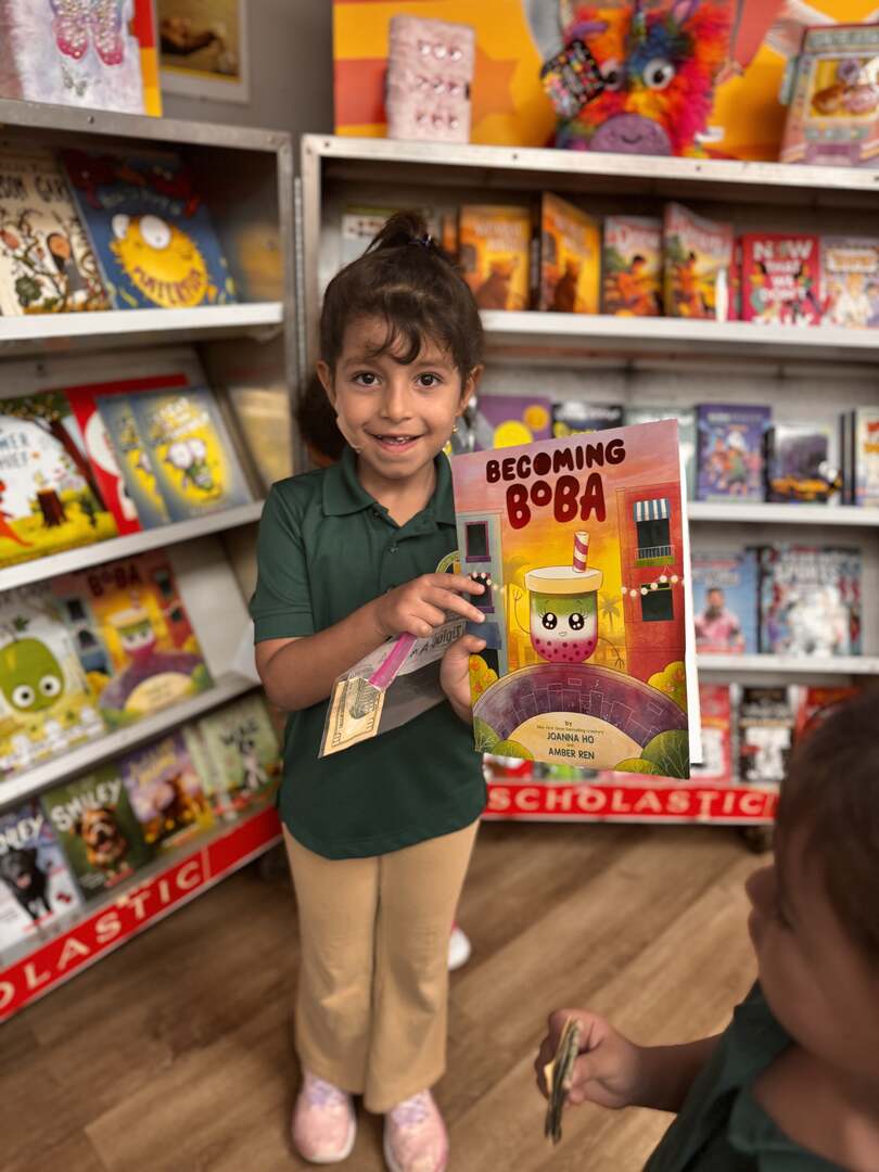A smiling student showing a picture book in front of the shelves