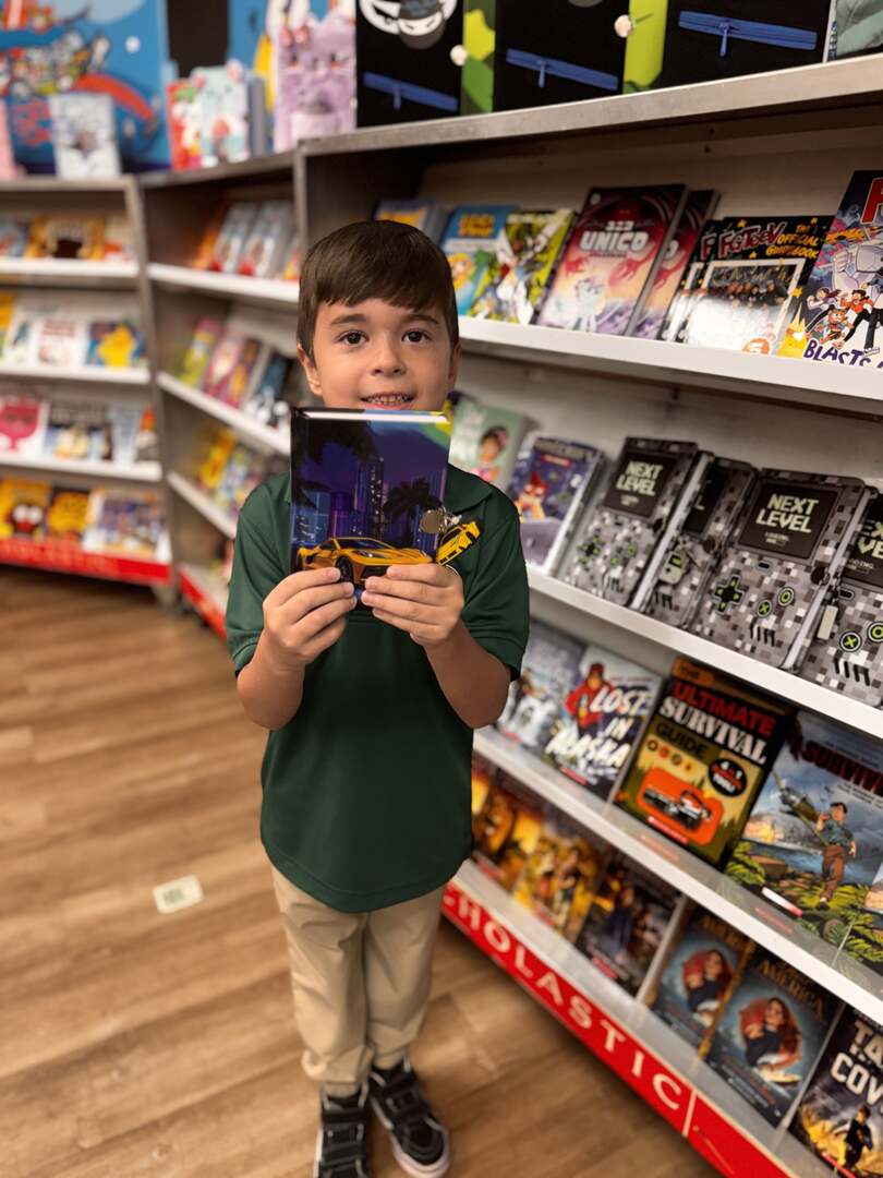 A student proudly holding up a chosen book by the shelves