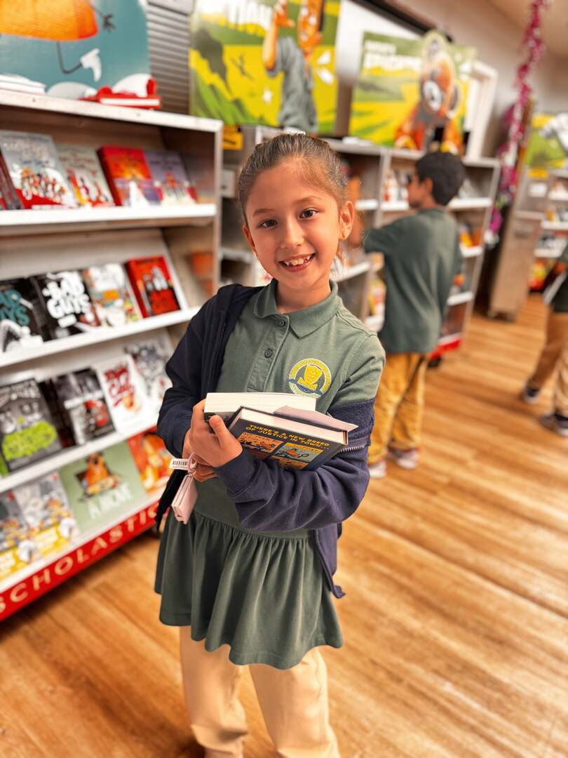 A smiling student carrying a stack of books