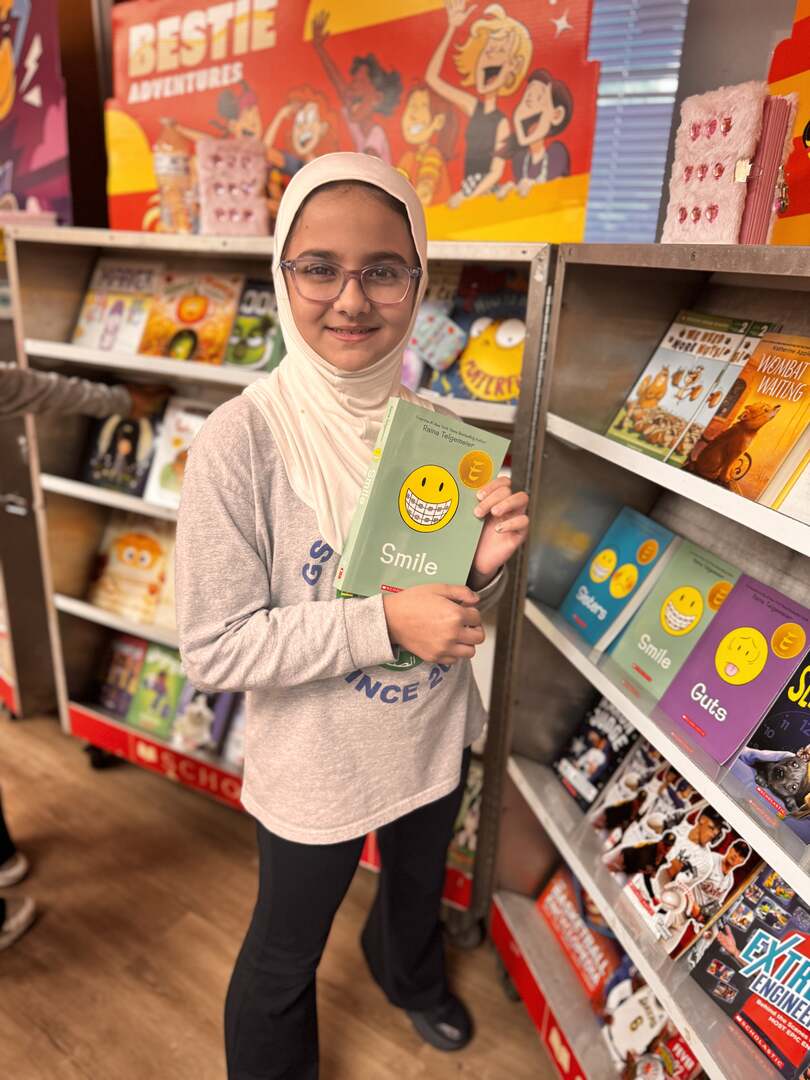A student holding a graphic novel beside the bookshelves