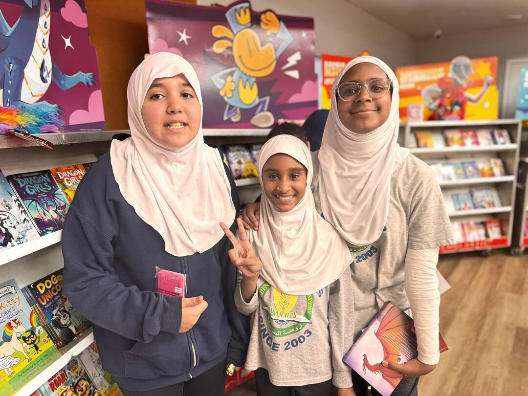 Three friends smiling together by the bookshelves