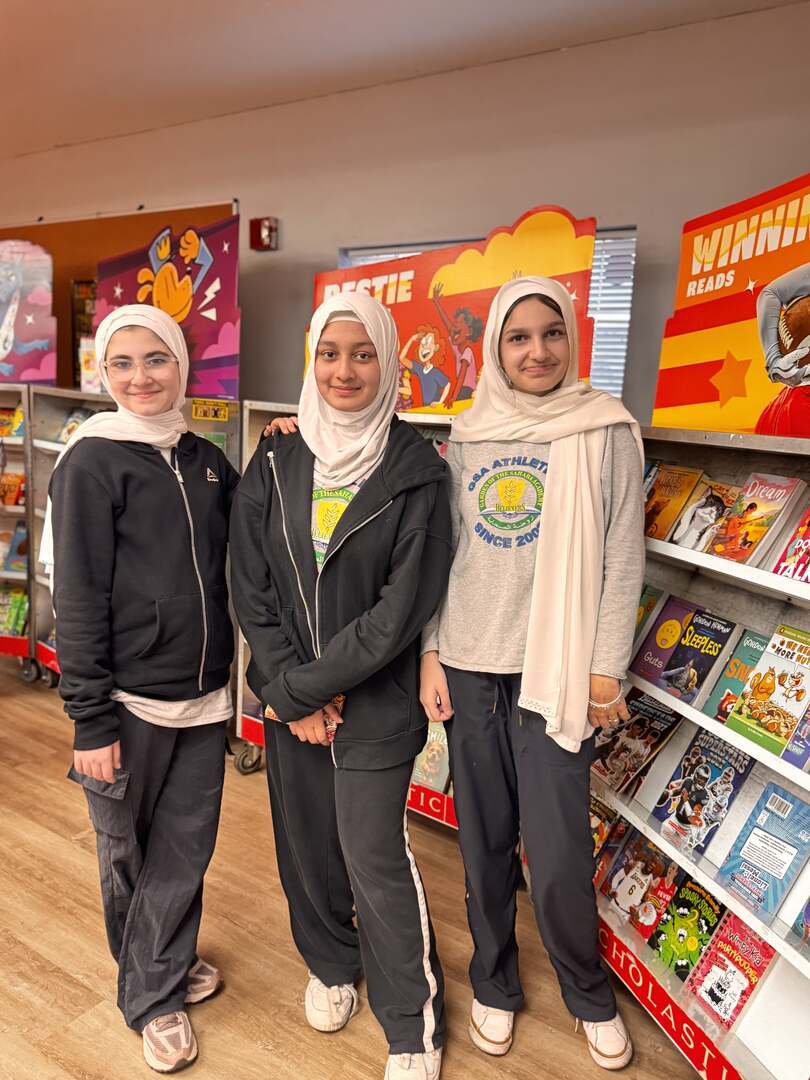 Three students posing beside the shelves of books