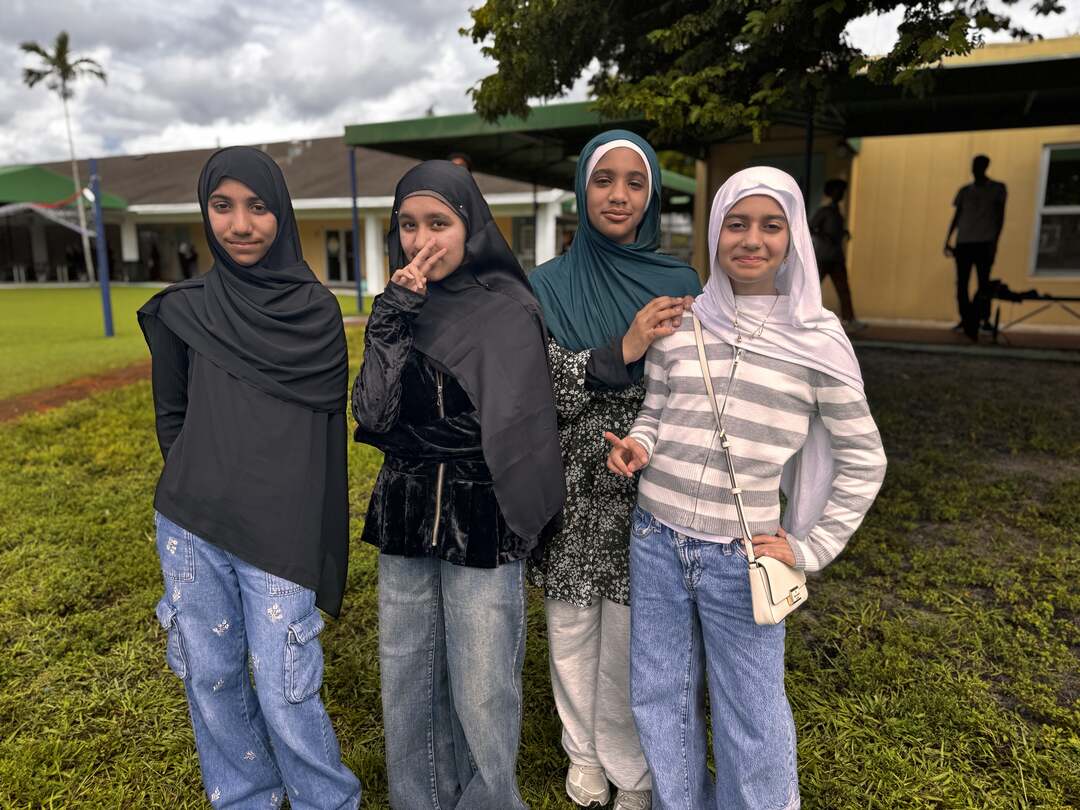 Four friends in dark and teal hijabs and a striped top pose on the lawn
