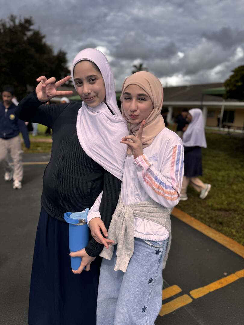 Two friends in soft pink and peach flash peace signs under cloudy skies