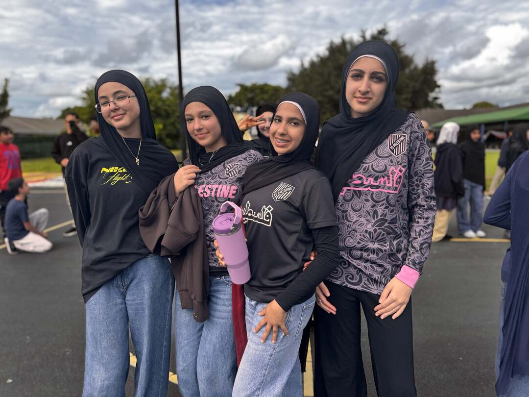Four friends in black hijabs and patterned tops smile together outside