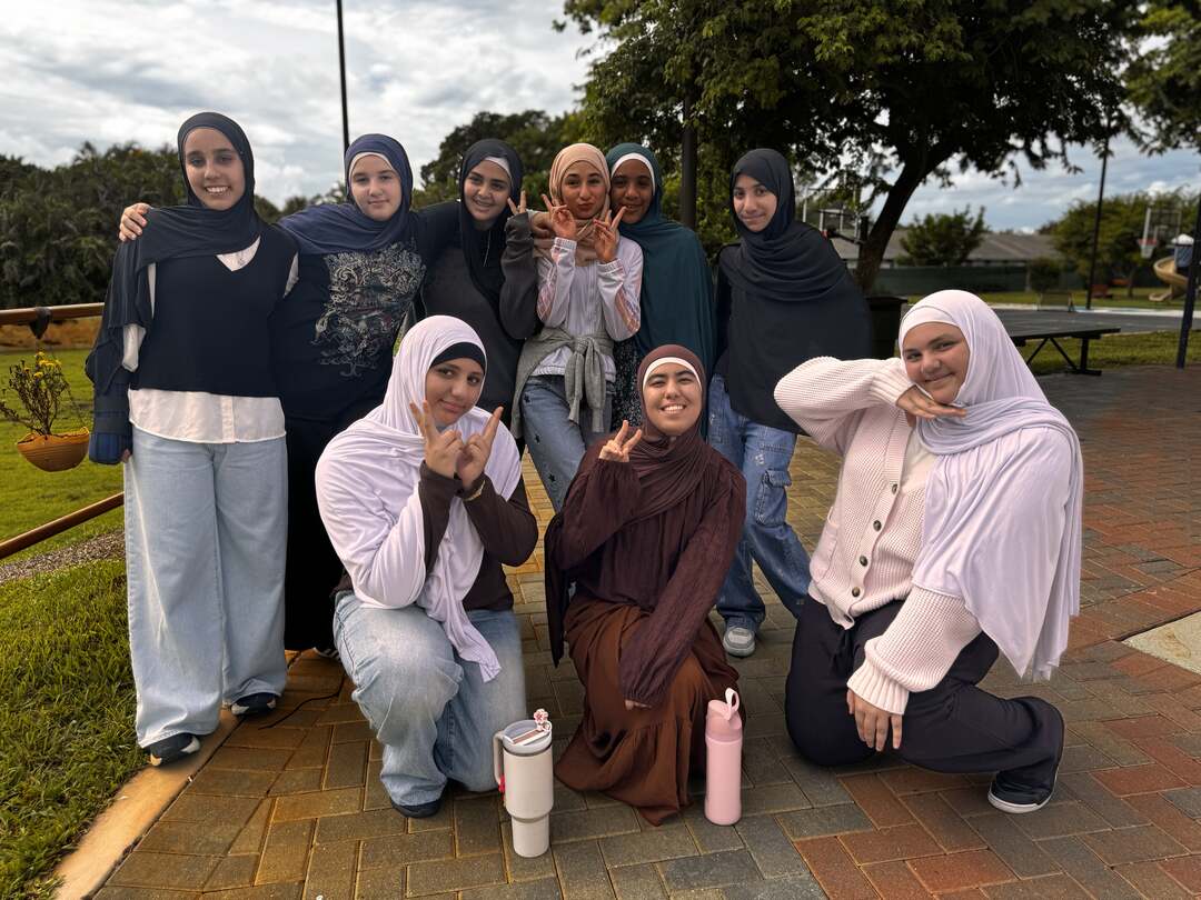 Friends in browns, creams and denim kneel and flash peace signs on the brick path