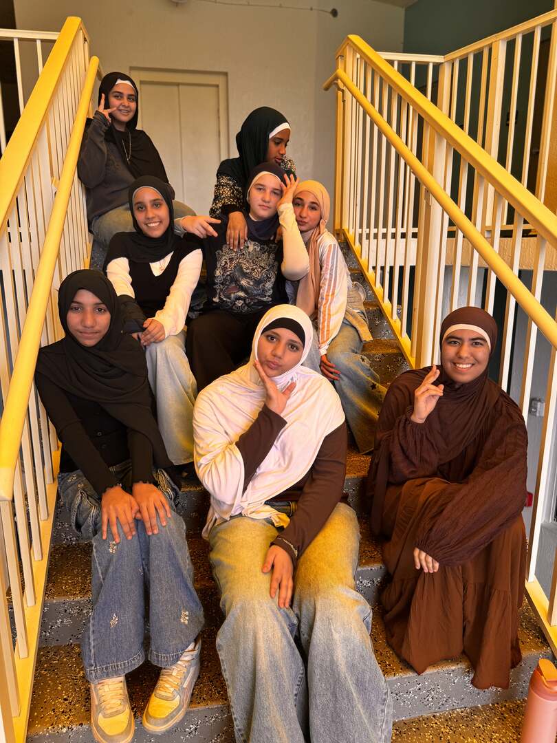 Students in warm browns, creams and denim pose together on the stairs for Dress Down Day