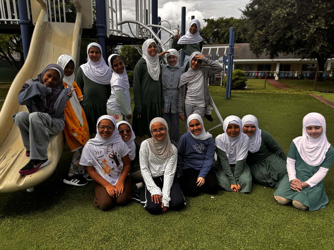 Smiling students in fall greens, golds and creams gather at the playground on Dress Down Day