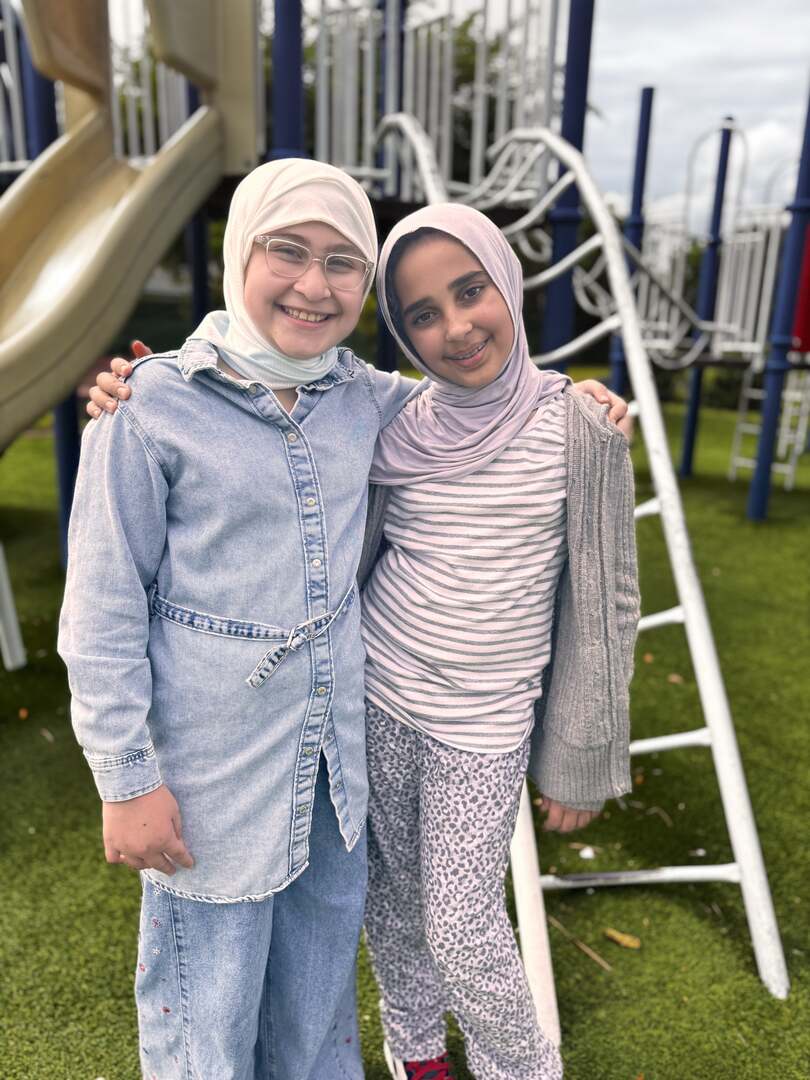 Two friends in denim and stripes share a hug by the slide