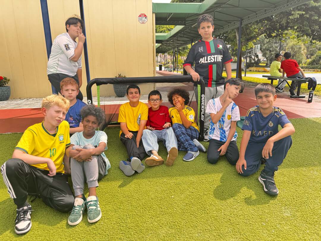 A crew of classmates in jerseys and bright tees gather around a mini soccer goal
