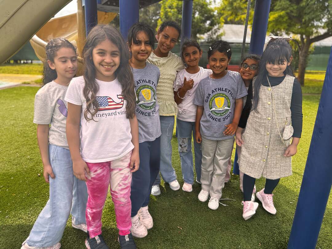 A cluster of smiling friends gathers under the playground on Dress Down Day