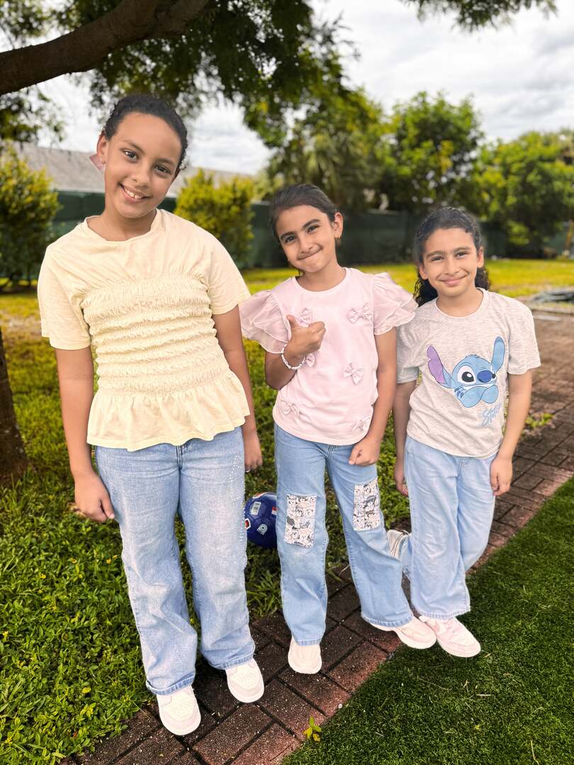 Three friends in soft cream and pink tops pose under the trees