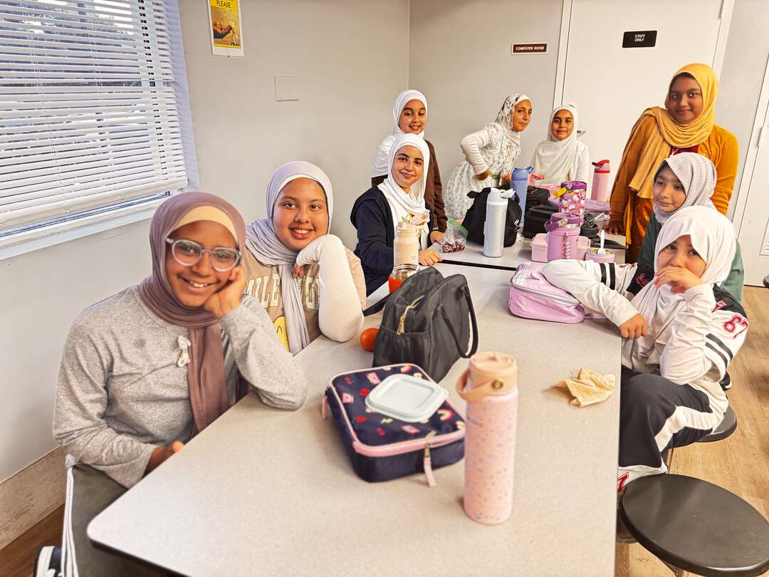 Classmates in mustard, mauve and cream smile around the lunch table