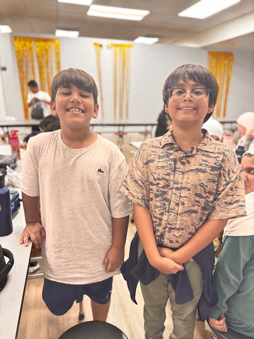 Two friends in a cream tee and patterned shirt grin in the lunchroom