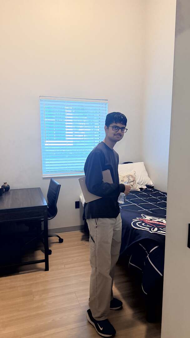 A student smiling inside a residence hall bedroom